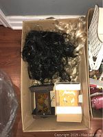 Box with two Halloween wigs (black and blonde) and a boxed lighted pumpkin candle decoration along with another small Halloween item in a box.