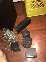 Four small black Samsung satellite speakers with wires on the floor