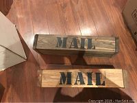 Photo showing two rectangular handcrafted wooden mailboxes with 'MAIL' stenciled on top in black, placed on wooden floor