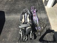 Two strollers side by side on black concrete; Peg Perego stroller on left with padded seat and second purple umbrella stroller with umbrella cover to the right.