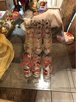 Photo showing 24 clear glasses with red and purple autumn leaf decorations, arranged on glass table.