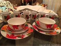 Front angled photo showing 6 autumn leaf decorated mugs and dinnerware: three large plates with bowls on top and multiple mugs in the background