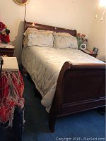 Full view of queen size wooden bed frame with mattress, light blue patterned bedding and pillows. Shows wear and scratches.