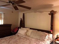 Dark wooden king size poster bed frame partially assembled with four tall carved posts, beige bedding and pillows visible.