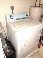 Full view of white front load dryer showing rust or dirt marks on top, placed beside a water heater.