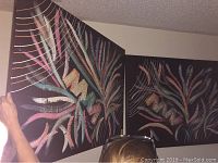 View of two large matching abstract oil paintings on canvas with colorful curved lines on black background, one framed and one unframed