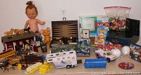 Wide shot showing the full variety of toys including the Pebbles doll, barn with horses, horse trailer, marbles, LEGO bricks, board games, Hot Wheels cars and other toys.