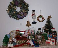 Full lot arranged on table with large decorated wreath hanging above. Includes figurines, miniature trees, wreaths, and assorted ornaments.