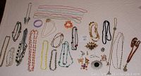 Top down view of assorted costume jewelry laid out on fabric, showing many necklaces, bracelets, brooches and pins arranged with varied colors and styles.