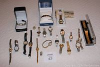 Top down view of all 18 assorted men's and women's wristwatches laid out on a cream colored fabric surface, with two watches in original boxes (Anne Klein II and Seiko).