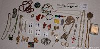 Overview of vintage costume jewelry assortment laid out on quilted surface, showing various necklaces, bracelets, earrings, brooches, and pins.