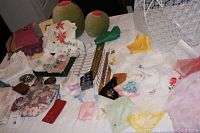 Wide view of assorted napkins, handkerchiefs, decorative pillows, folded linens, scarves, and vintage aprons arranged on a bed