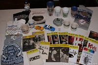 Overview photo showing assorted New York City memorabilia including mugs, cups, model cars, merchandise, and Playbills arranged on a dark surface.