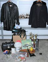 Full view of assorted vintage and modern home goods including clothing, shoes, doctor's bag, fans, trophies, and cameras arranged on garage shelving and floor.