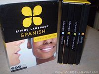 Living Language Spanish Complete Edition box with 4 black cases labeled Essential, Intermediate, Advanced, and Audio Textbook.