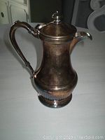 Photo shows tarnished silver plated coffee or tea pot with lid closed, curved handle and spout, standing approx. 8 inches tall.