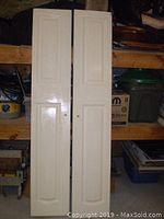 Two side-by-side paneled closet or pantry doors leaning against shelving, showing full door design and attached knobs.