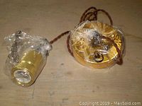 Close-up of a single light socket and mounting plate with protective plastic wrap, showing the copper or brass finish and braided cord.