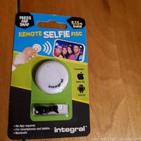 Single Integral Remote Selfie Disc button in unopened blister pack with packaged USB cable, showing front packaging branding and usage information.