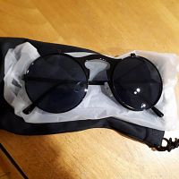 Black steampunk glasses with round dark tinted lenses resting on white dust rag and black pouch