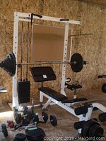 Assembled bench press rack system with weight bench, preacher pad, leg rollers, weight stack, loaded barbell and plates on floor
