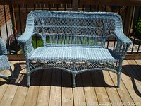 Front view of the blue wicker loveseat showing entire piece in natural light outside on wooden deck.