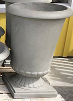 Gray urn-style planter with rolled rim, fluted stem and square pedestal base, shown on pallet