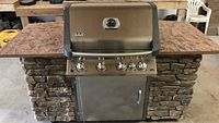 Front view of outdoor kitchen island with closed Napoleon grill, stone veneer base, wood panel front and composite countertop