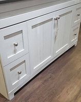 Front view of the full vanity base showing drawers, doors and knobs against wood-look floor.