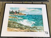 Framed watercolor painting showing full landscape scene including lighthouse, rocky shore, and sailboat.