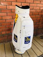 Front view of white RBC golf bag showing sponsor logos, side pocket with signatures