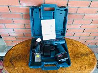 Open case displaying Bosch cordless drill kit including drill, battery, charger, drill bits, and manual arranged inside.