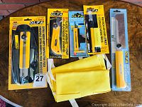 Overview of all OLFA cutting tools and accessories in original packaging on table.