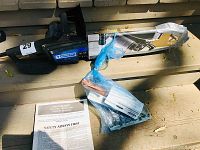 Photo showing the electric chainsaw with Mastercraft branding, a protective blade cover, owner's manual, and a bag of accessories tied in blue plastic.