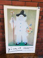 Full view of the framed Picasso art show poster with brick wall background, showing the entire figure and frame.