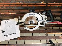 Full view of the Black and Decker worm drive saw with the attached blade and instruction manual placed next to it.