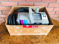 Campbell Hausfeld Powerpal air compressor pump placed inside a cardboard box with power cord coiled beside it. Side view showing control knob and colored label sticker with operating instructions.