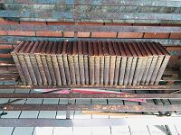 Full 24 volume set of 1910 Encyclopedia Britannica with leather bound covers and gilded spines placed on a metal bench in front of a brick wall.