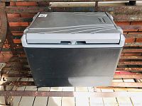 Front view showing cooler closed on bench against brick wall, with gray lid and black body.