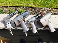 Four air tools laid out on a surface showing the overall lot including the impact wrench, drill, and nail gun