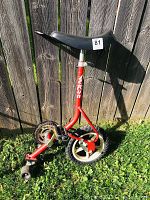 Front view of the vintage Lerun training unicycle showing the single main white rimmed wheel with a knobby tire, pedals with reflectors, and black training wheels at the rear on a red frame with Lerun branding on the seat post.