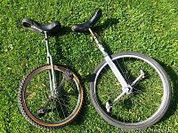 Photo of two unicycles on grass showing side view, one with knobby tire and one with smooth tire.