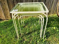 Three vintage nesting tables stacked together showing the largest table with glass top and wrought iron frame