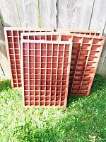 Multiple vintage wooden printers trays leaning against a fence outdoors on grass, showing small divided compartments