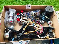 Box with assorted trailer hitch balls, hitches, bungee cords, wiring connectors, Reese towing product, and rubber hitch covers.