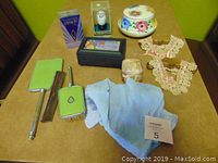 Overview of all items on a table including perfume, boxes, lace collars, scarf, brush and mirror set.