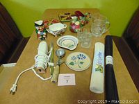 Top view of assorted kitchen items including 4 creamers, electric knife, glassware, scoops, decorative plates and liners displayed on a brown surface.