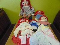 Four Raggedy Ann and Andy dolls with various clothing, showing signs of wear and some stains.