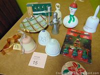 Photo showing lot of various Christmas items including Lladro and Hummel bells, a snowman gourd, musical bell, Department 56 lighted street lamp set, and decorative plate.