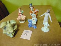 Overview of all six figurines including clown, girls, angel, lamb, and gargoyle on a surface with a green wall background